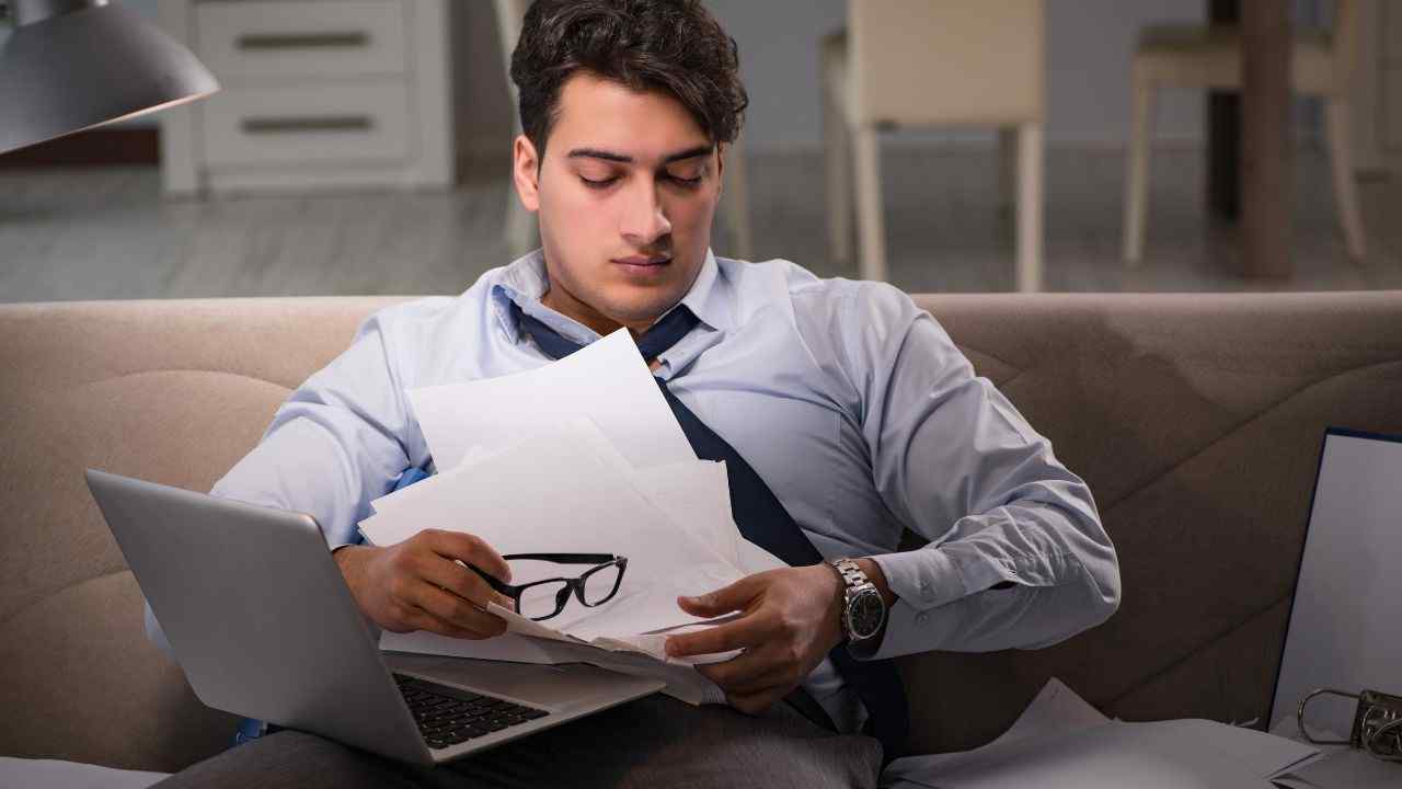 Hombre sentado lleno de papeles y unos espejuelos como confundido y abrumado